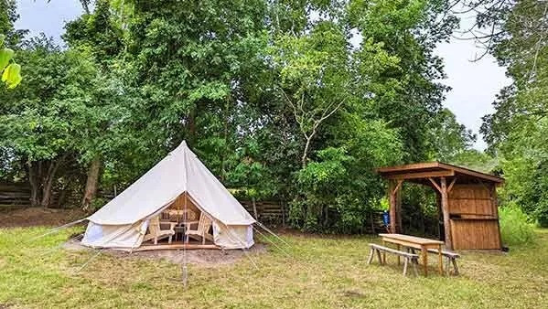 White prospector style tent in nature, beside a wood structure/outdoor kitchen and seating