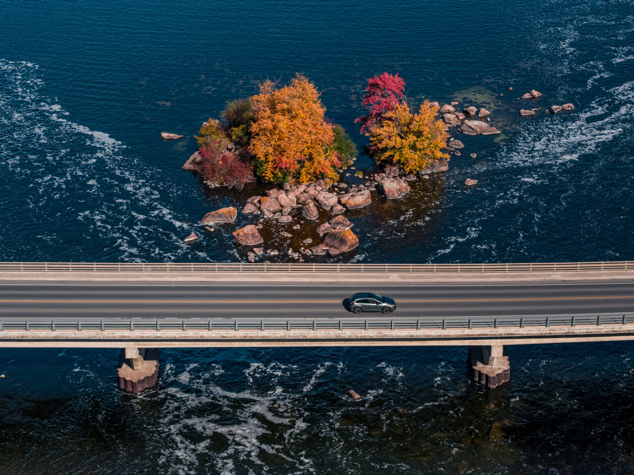 Aerial image of Car driving along a bridge in Buckhorn Fall Drive Colourful Island of fall trees in background