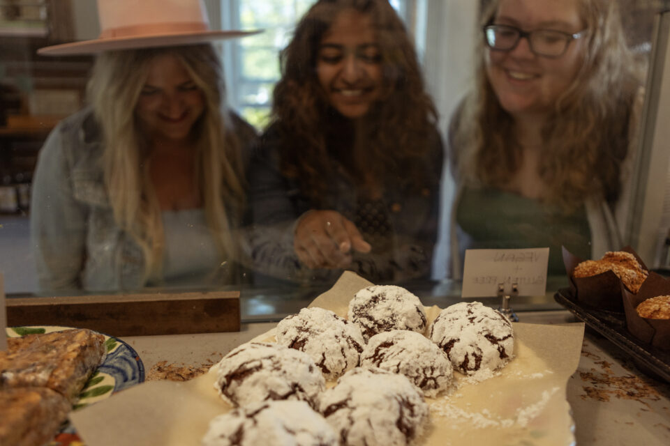 Friends eyeing up baked goods in a display case, baked goods in the foreground of the photo.