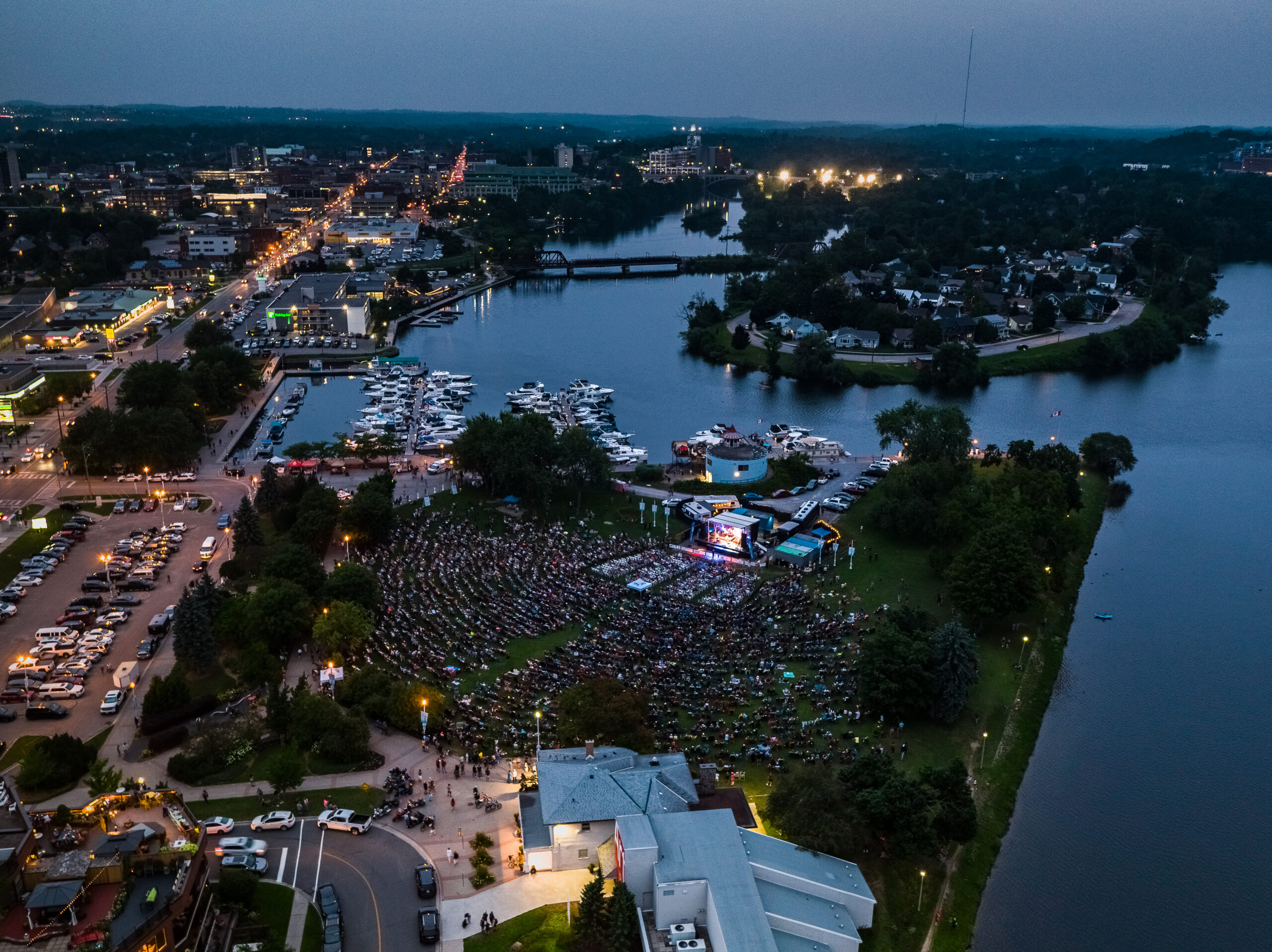 Aerial photograph of Peterborough Musicfest, with concert crowd in the foreground and marina, lakes and city in the background.