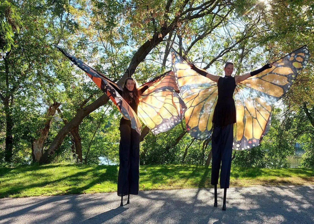 TWO PEOPLE IN A PARK ON STILTS WITH BUTTERFLY WINGS