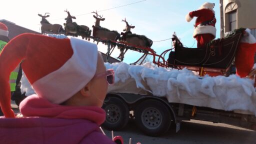 Profile photo of a child in a santa hat with sun glasses looks up at Santa's arrival at the Lakefield Santa Claus parade.