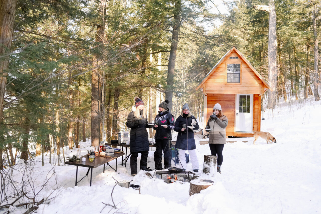 A group of people standing in front of a small bunkie in winter