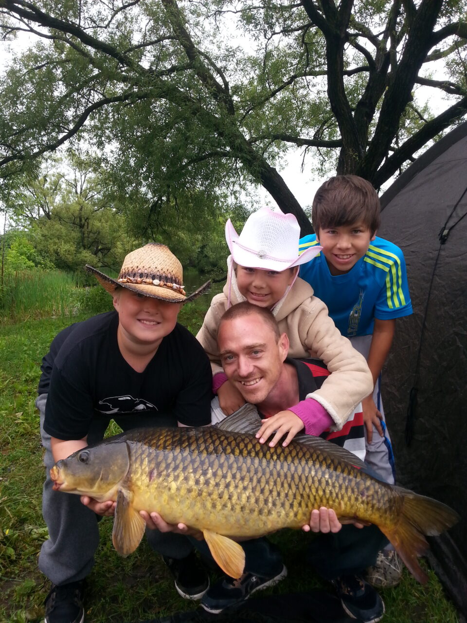 A man holding a fish with 3 children smiling beside him