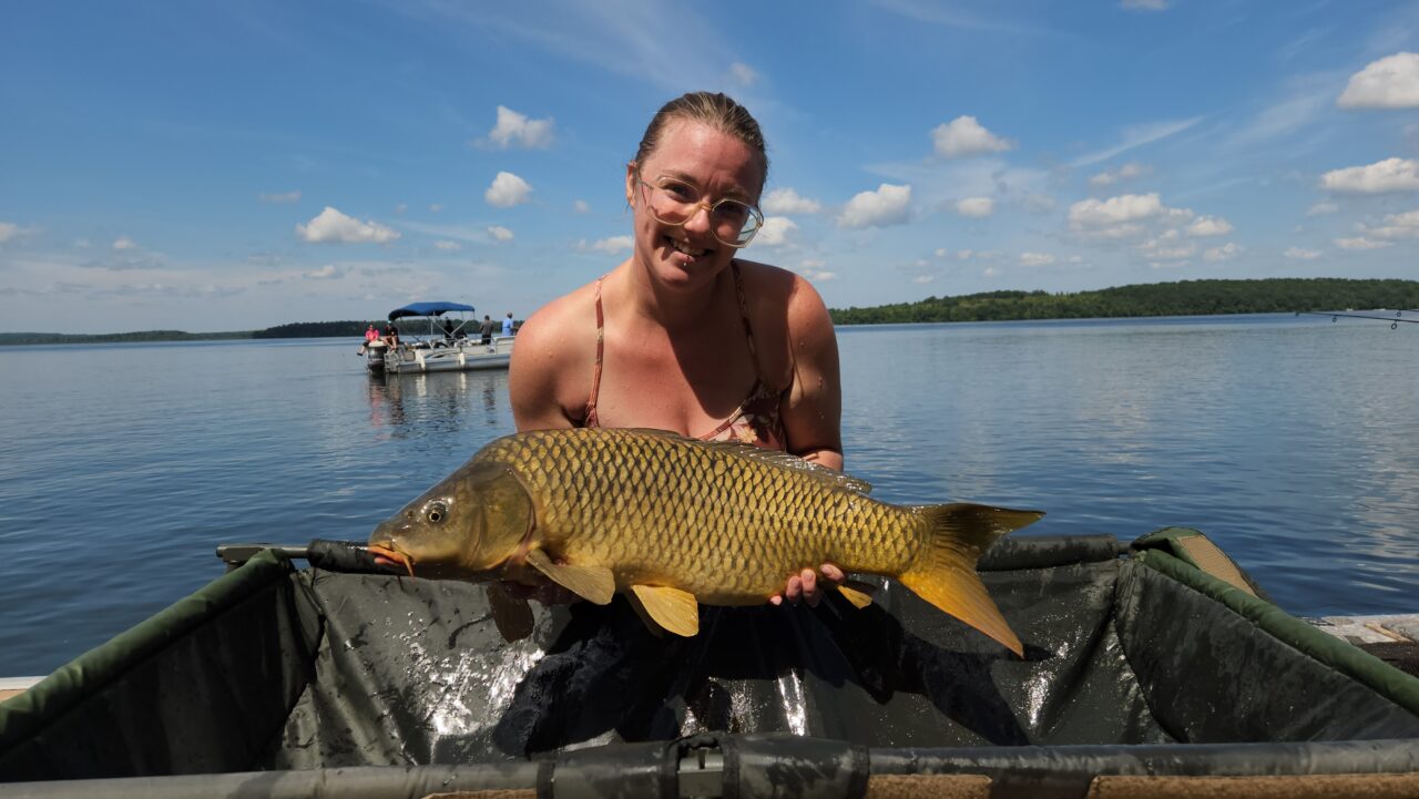 A woman holding a large fish in front of a lake