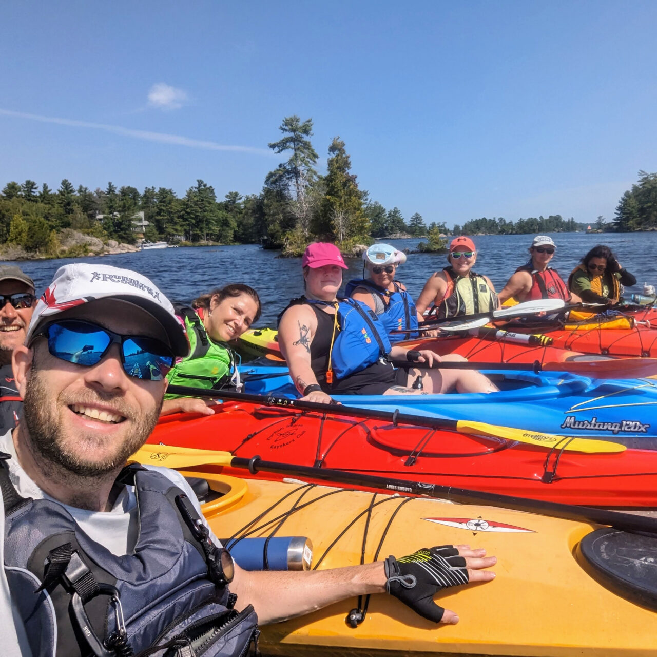 A group of people in colourful kayaks, smiling at the camera