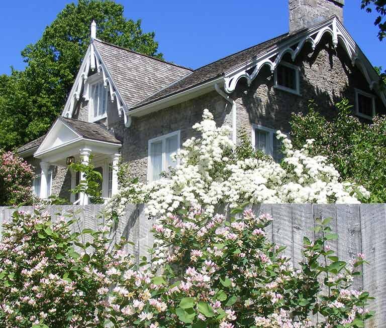 Hutchison House Museum in Peterborough Ontario - limestone cottage with white picket fence with flowers in full bloom.